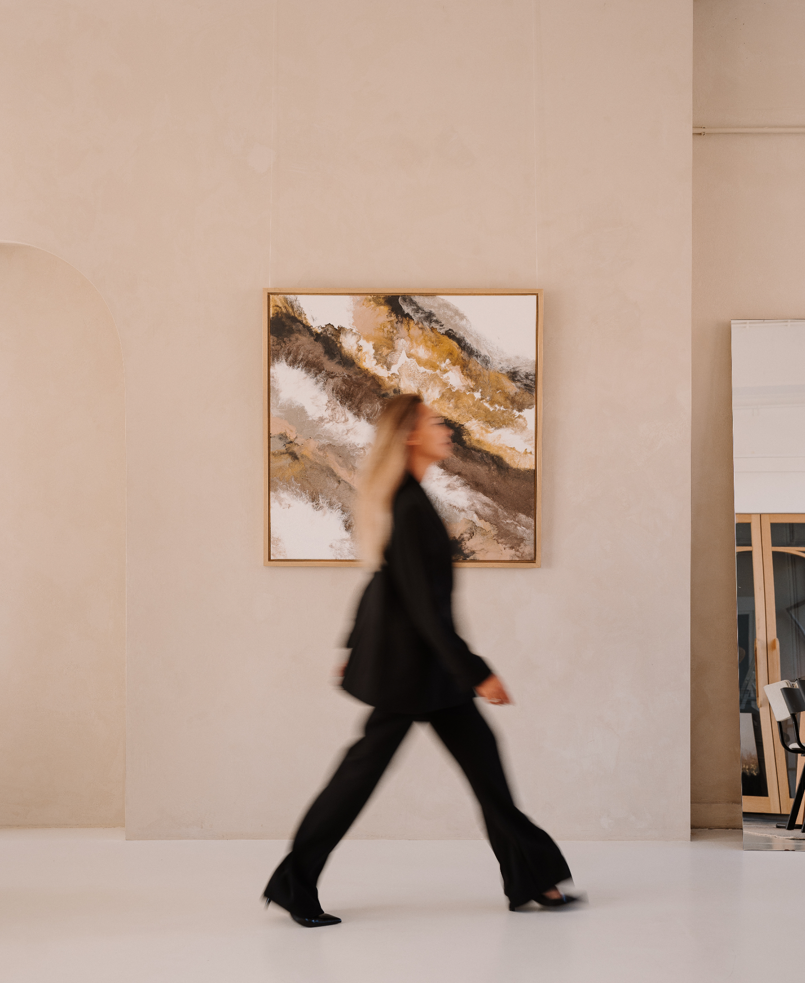 Michelle Daisy loopt langs een groot abstract schilderij in een verfijnde, lichte ruimte.