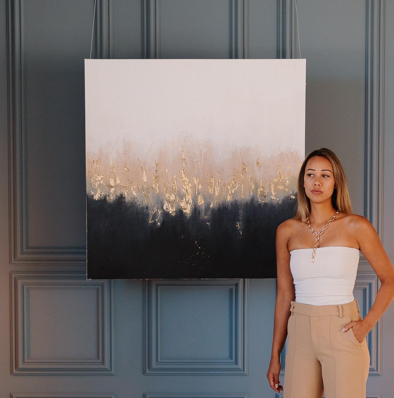 Michelle Daisy naast een goudgeaccentueerd schilderij in een verfijnd interieur.